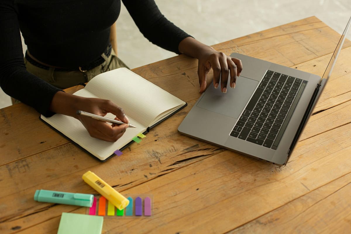 A woman is using her laptop and writing notes.